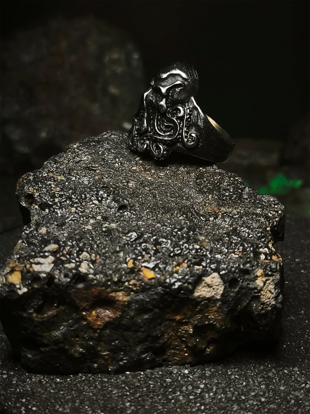 La Faz de Cthulhu: Vista lateral de anillo soberano del abismo de acero inoxidable sobre roca volcánica estilo dark en Chile.