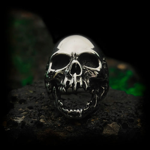 Anillo calavera gótico de acero El Clamor de Baudelaire, mandíbula abierta en vista frontal sobre roca | Abyssal Relics.