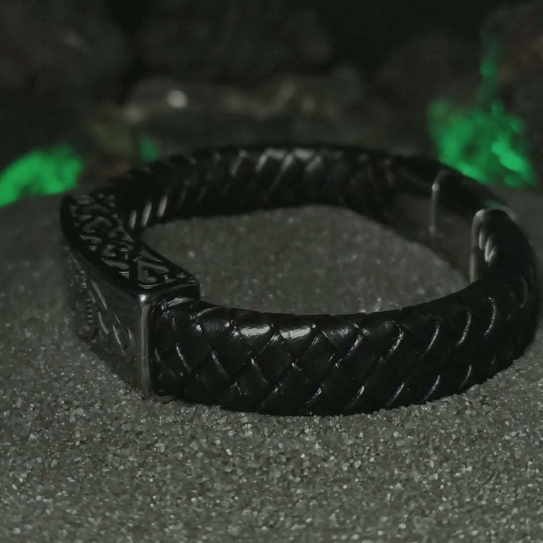 Video del brazalete vikingo Vegvísir de acero inoxidable y cuero sintético negro sobre arena oscura entre humo místico.